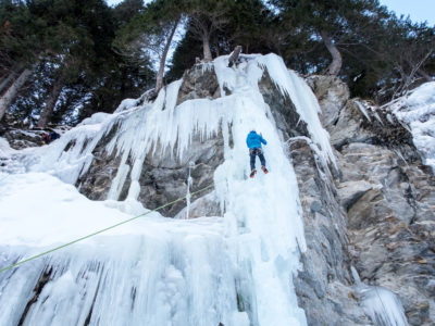 Steile Eiszapfen und Eisformationen mit Eiskletterer und Felswand.