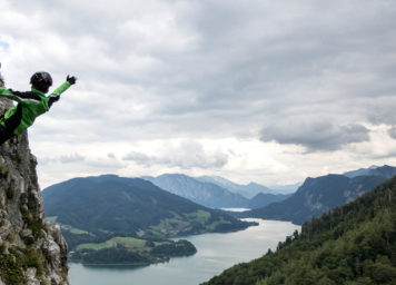 Thumbnail http://Kind%20streckt%20am%20Klettersteig%20Hände%20in%20die%20Luft%20mit%20See%20im%20Hintergrund