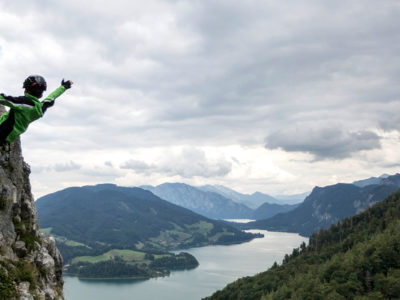Kind streckt am Klettersteig Hände in die Luft mit See im Hintergrund
