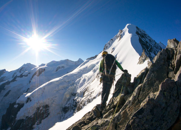 Bergsteiger im Sonnenschein vor schneebedecktem Gipfel
