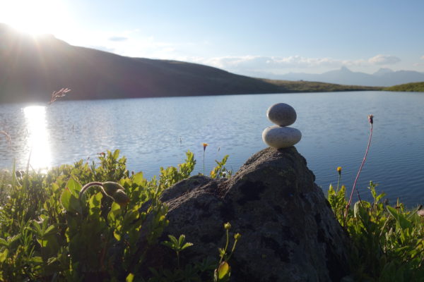 Steinmann übereinander mit Sonne und See in Balance und Ruhe