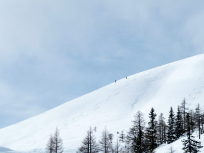 Skitourengeher und Abfahrtsspuren im Schnee mit Wedelspur
