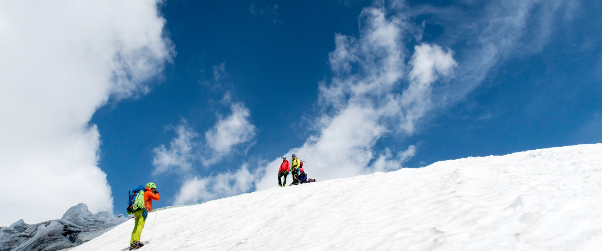 Person wird an einem Firnanker eine Firnflanke abgelassen und gesichert.